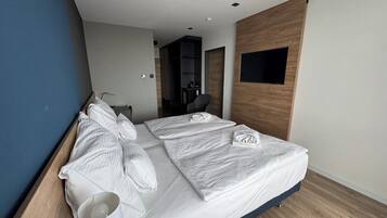 A modern hotel room with a large bed, a desk, and a flat-screen TV mounted on the wall.