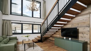 Una sala de estar moderna con una escalera, un sofá verde, una mesa de centro de madera y un televisor de pantalla plana sobre un mueble verde.