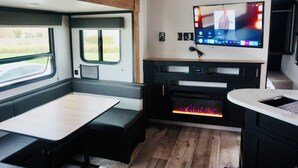 A compact RV interior with a kitchenette, a flat-screen TV mounted above the counter, and a bench seating area. - Toy Hauler Vengence Rouge (Brentwood)