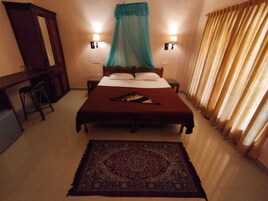 Habitación de hotel con cama, escritorio, silla, mesita de noche, lámpara y ventana con cortinas.