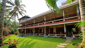 A two-story building with a covered outdoor area, palm trees, and a well-maintained lawn. - HOTEL COCO BECH KOVALAM AYURVEDIC RESORT (Kovalam)