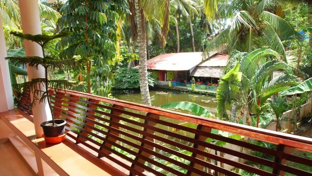 A wooden balcony with a view of a water body and lush greenery. - HOTEL COCO BECH KOVALAM AYURVEDIC RESORT (Kovalam)