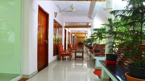 A spacious hallway with a polished floor, wooden doors, and a seating area with chairs and potted plants. - HOTEL COCO BECH KOVALAM AYURVEDIC RESORT (Kovalam)