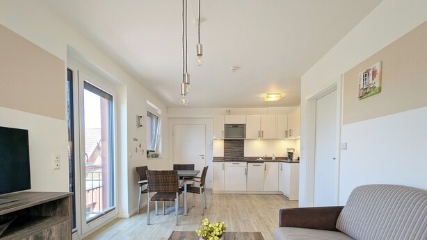 A modern living room with a sofa, a coffee table with flowers, a TV, and a dining area with chairs and a table.