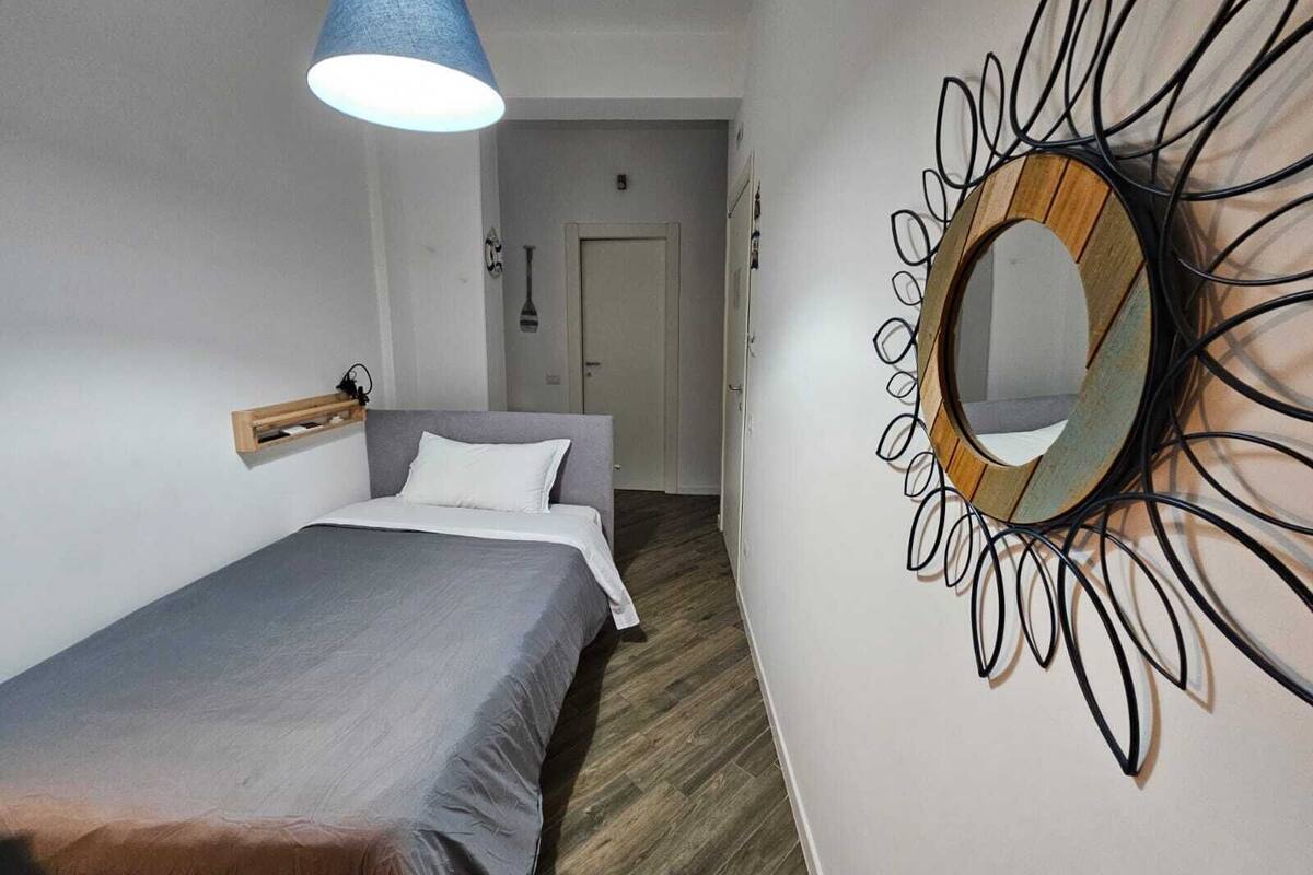A bedroom with a bed, a hanging light fixture, and a wall-mounted mirror.