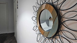 A hallway with a round mirror with a wooden frame and black metal spirals. - Guest House Colors - by Be Your Home (Civitavecchia)