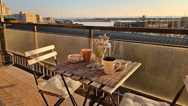 A balcony with a table set for two, overlooking a marina with boats and buildings. - Guest House Colors - by Be Your Home (Civitavecchia)