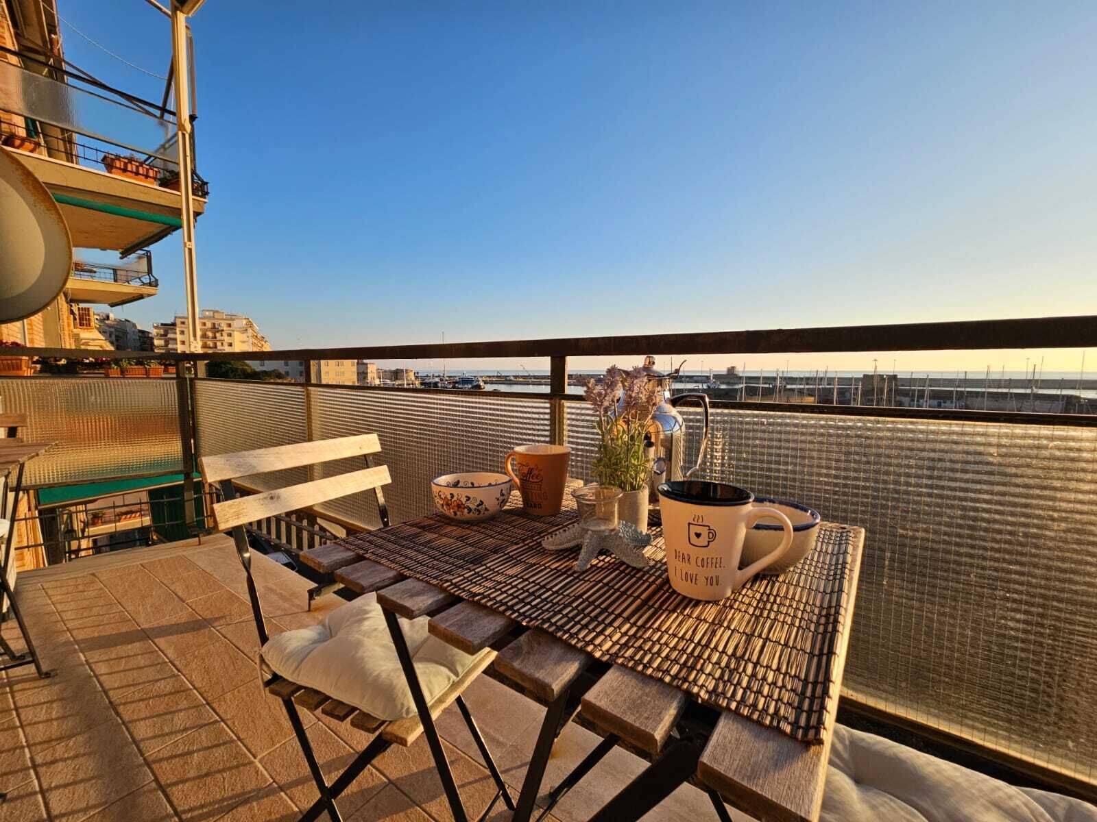 Un balcon avec une table dressée pour deux personnes, une chaise, une tasse à café et une plante en pot.