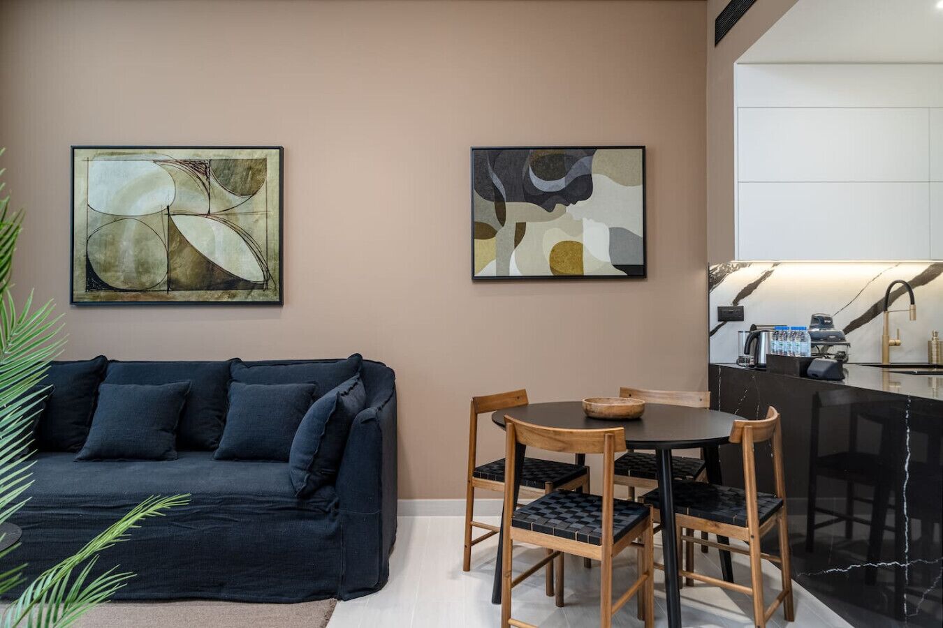 A modern living room with a dark blue sofa, wooden chairs, and abstract art on the walls.