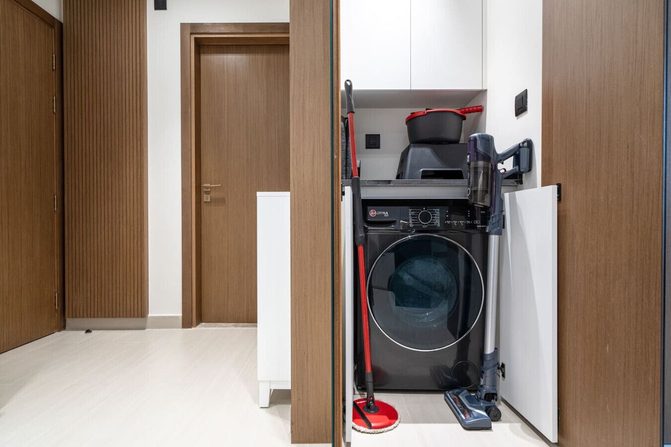 A compact laundry room with a washing machine, a vacuum cleaner, and a mop.