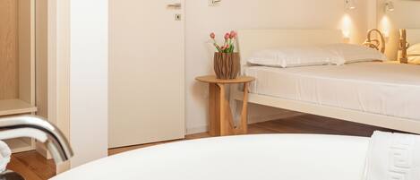 A hotel room with a bed, a small wooden table with a vase of flowers, a round white table, and a white chair.