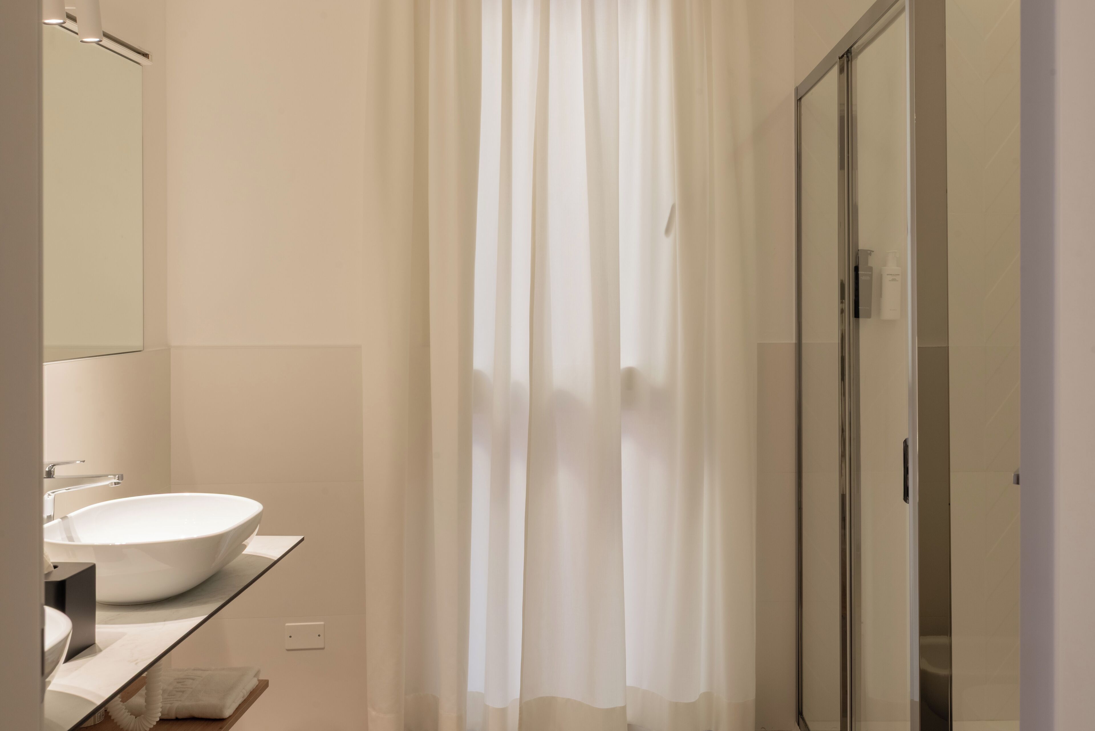 Une salle de bain moderne avec un grand lavabo blanc, une cabine de douche en verre et un rideau de douche translucide.