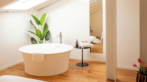 A modern bathroom with a freestanding bathtub, a small table with toiletries, and a potted plant. - Palazzo Sant'Agostino by The First (La Spezia)