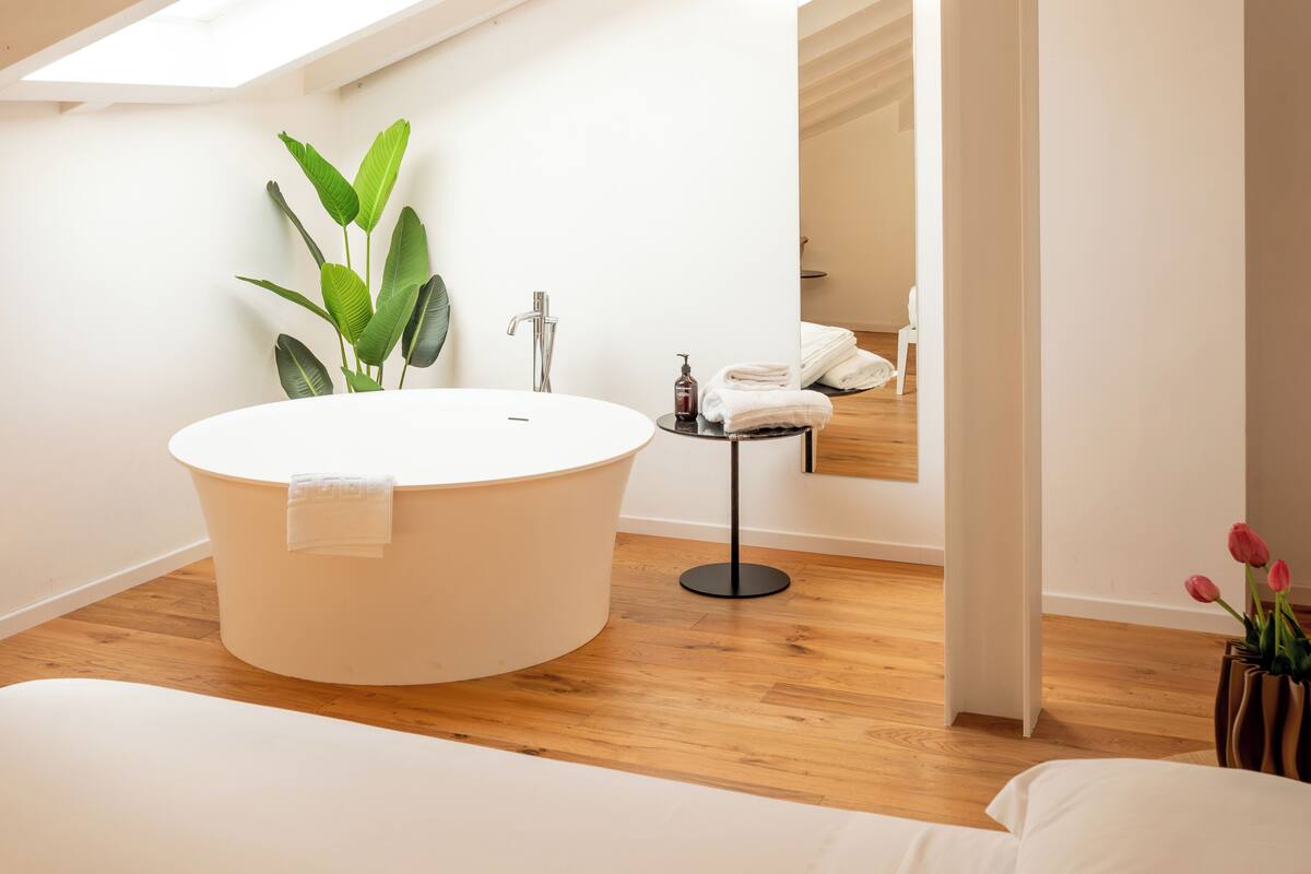 A modern bathroom with a freestanding bathtub, a small table with toiletries, and a potted plant.