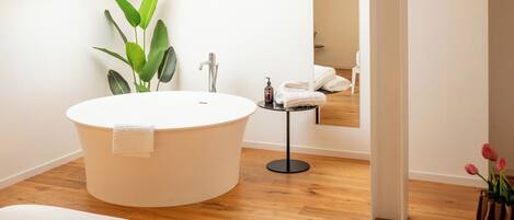 A modern bathroom with a freestanding bathtub, a small table with toiletries, and a potted plant.