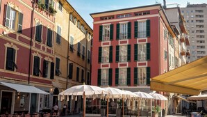 A courtyard with outdoor seating and a café, surrounded by buildings with balconies and shutters. - Palazzo Sant'Agostino by The First (La Spezia)