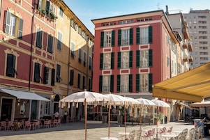 Un patio con mesas al aire libre y un café, rodeado de edificios con balcones y persianas.