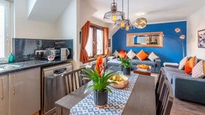 Une cuisine moderne avec un coin repas, un mur d’accent bleu et un salon doté d’un canapé et de coussins décoratifs.
