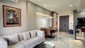 Ein modernes Wohnzimmer mit einer Couch, einem Esstisch mit Stühlen, einer Küchenzeile mit Kühlschrank und einem gerahmten Kunstwerk an der Wand.