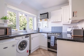 Une cuisine compacte équipée d’un lave-linge, d’un four à micro-ondes, d’une cuisinière et d’une fenêtre donnant sur les arbres.