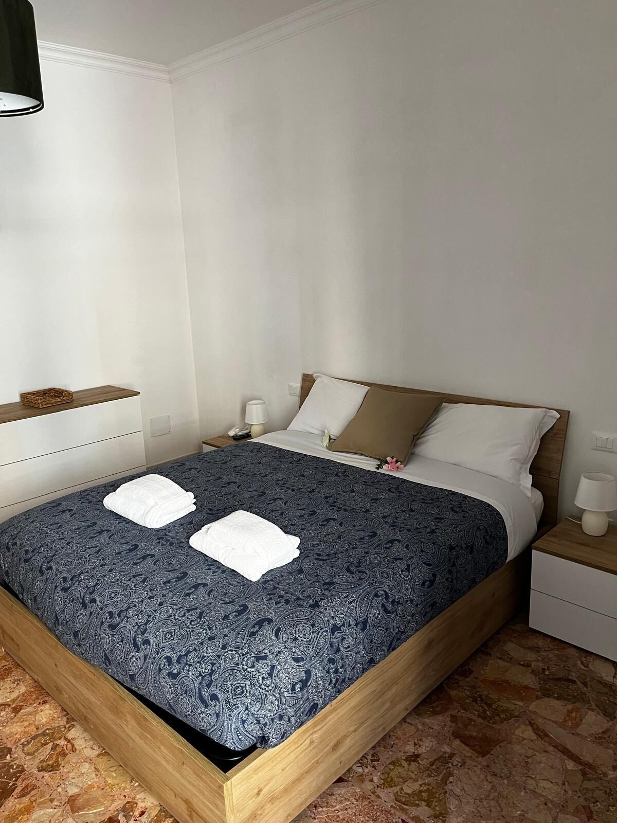 A neatly made bed with a patterned bedspread, two white towels, and a wooden headboard.
