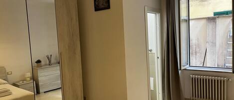 Une chambre moderne avec une grande armoire, une table de chevet avec une lampe, une fenêtre avec des rideaux et un radiateur.