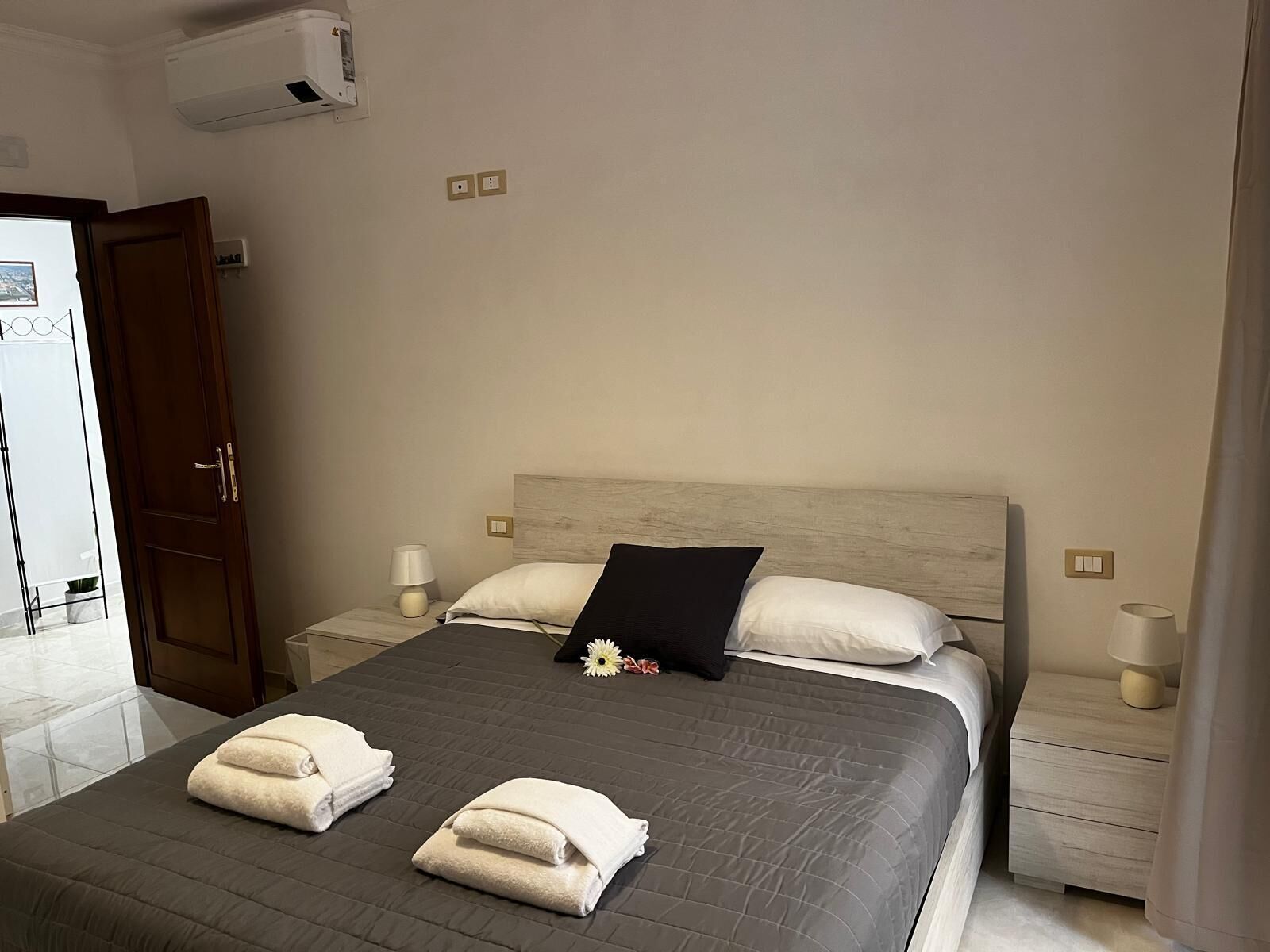 A hotel room with a large bed, two bedside tables, a wooden headboard, and a door to the left.