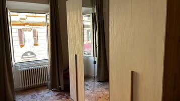 A room with a radiator, a window with shutters, and a view of a building outside.