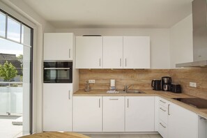 A modern kitchen with white cabinets, a wooden countertop, a built-in oven, and a coffee maker.