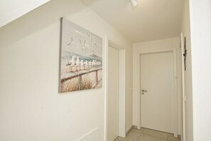 A hallway with a white door, a white wall, and a painting of seagulls on a pier.