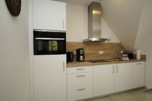 A modern kitchen with white cabinets, a built-in oven, a stainless steel range hood, and a wooden countertop.