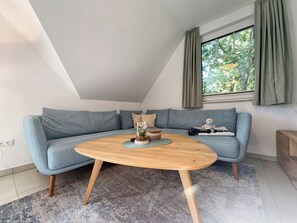 A modern living room with a light blue sofa, a wooden coffee table, and a view of greenery through a window. - Beachfront vacation rental with a balcony; access to the pool and sauna - Rex Rugia - Rex Rugia (Göhren)