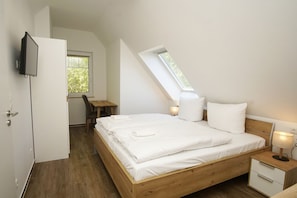 A bedroom with a sloped ceiling, a wooden bed, a desk, and a TV mounted on the wall.