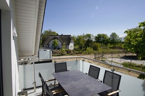 A balcony with a table and chairs, overlooking a garden with a house in the background. - Beachfront vacation rental with a balcony; access to the pool and sauna - Rex Rugia - Rex Rugia (Göhren)