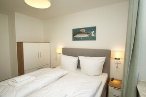 A hotel room with a bed, two bedside tables with lamps, a wardrobe, and a wall-mounted artwork of a fish. - Beachfront vacation rental with a terrace, access to the pool and sauna - Rex Rugia H-1010 - (Göhren)