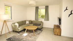 A modern living room with a sectional sofa, a wooden coffee table, a floor lamp, and a TV mounted on the wall.
