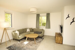 Een moderne woonkamer met een modulaire bank, een houten salontafel, een vloerlamp en een aan de muur bevestigde televisie.