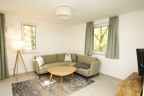 A modern living room with a sofa, a coffee table, a floor lamp, and a TV stand. - Beachfront vacation rental with a terrace, access to the pool and sauna - Rex Rugia H-1010 - (Göhren)