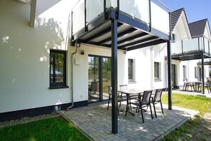 A modern outdoor patio with a table and chairs, a covered seating area, and a glass door leading to a garden. - Beachfront vacation rental with a terrace, access to the pool and sauna - Rex Rugia H-1010 - (Göhren)