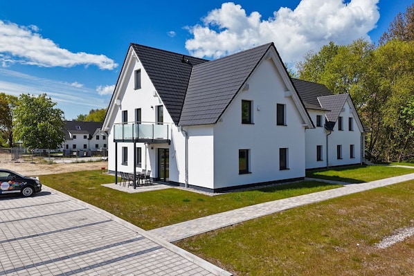 A modern two-story house with a balcony, a paved driveway, and a well-maintained lawn.