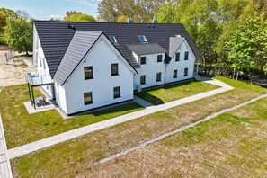 A modern two-story house with a symmetrical design, featuring a central entrance and a covered outdoor seating area. - Beachfront vacation rental with a terrace, access to the pool and sauna - Rex Rugia H-1010 - (Göhren)