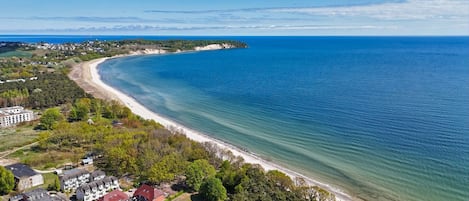 Vista aérea de una zona costera con una extensa playa de arena, edificios residenciales y abundante vegetación.