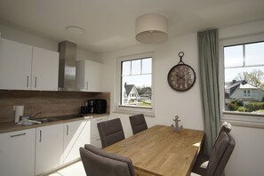 A modern kitchen with white cabinets, a wooden countertop, a dining table with four chairs, and a large window with a view of houses. - Beachfront vacation rental with a balcony; access to the pool and sauna - Rex Rugia - Rex Rugia (Göhren)