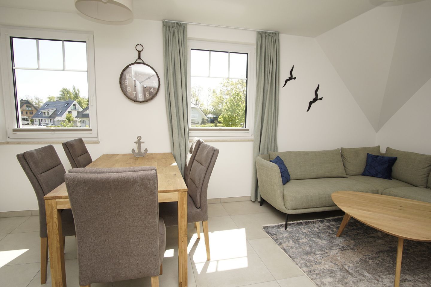 A living room with a dining table, chairs, a sofa, a coffee table, and a large window with curtains.