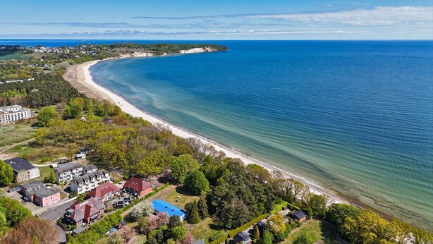 Ett flygbildsbild av ett kustområde med en lång sandstrand, bostadshus och frodig grönska.