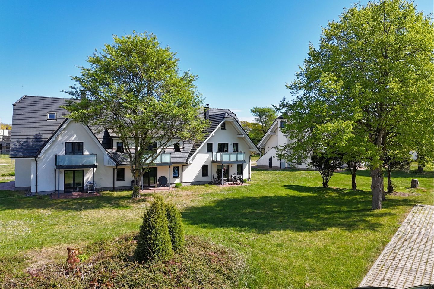 A modern residential building with a symmetrical design, featuring a central entrance, a covered patio, and a well-maintained lawn.