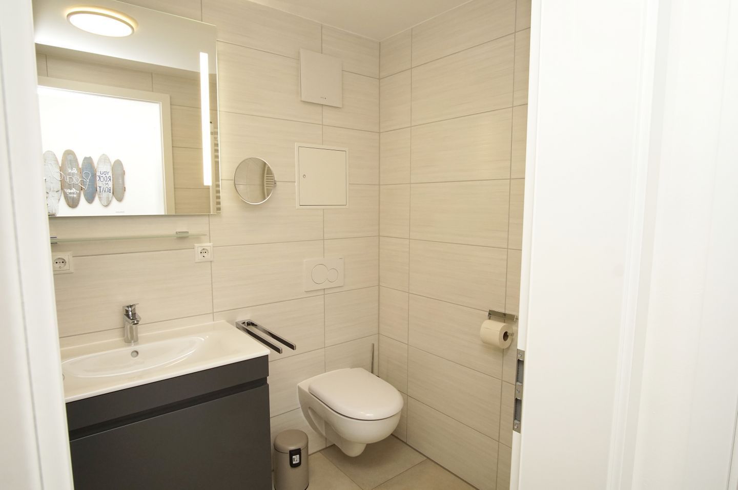 Une salle de bain moderne avec un lavabo blanc, des toilettes et un miroir.