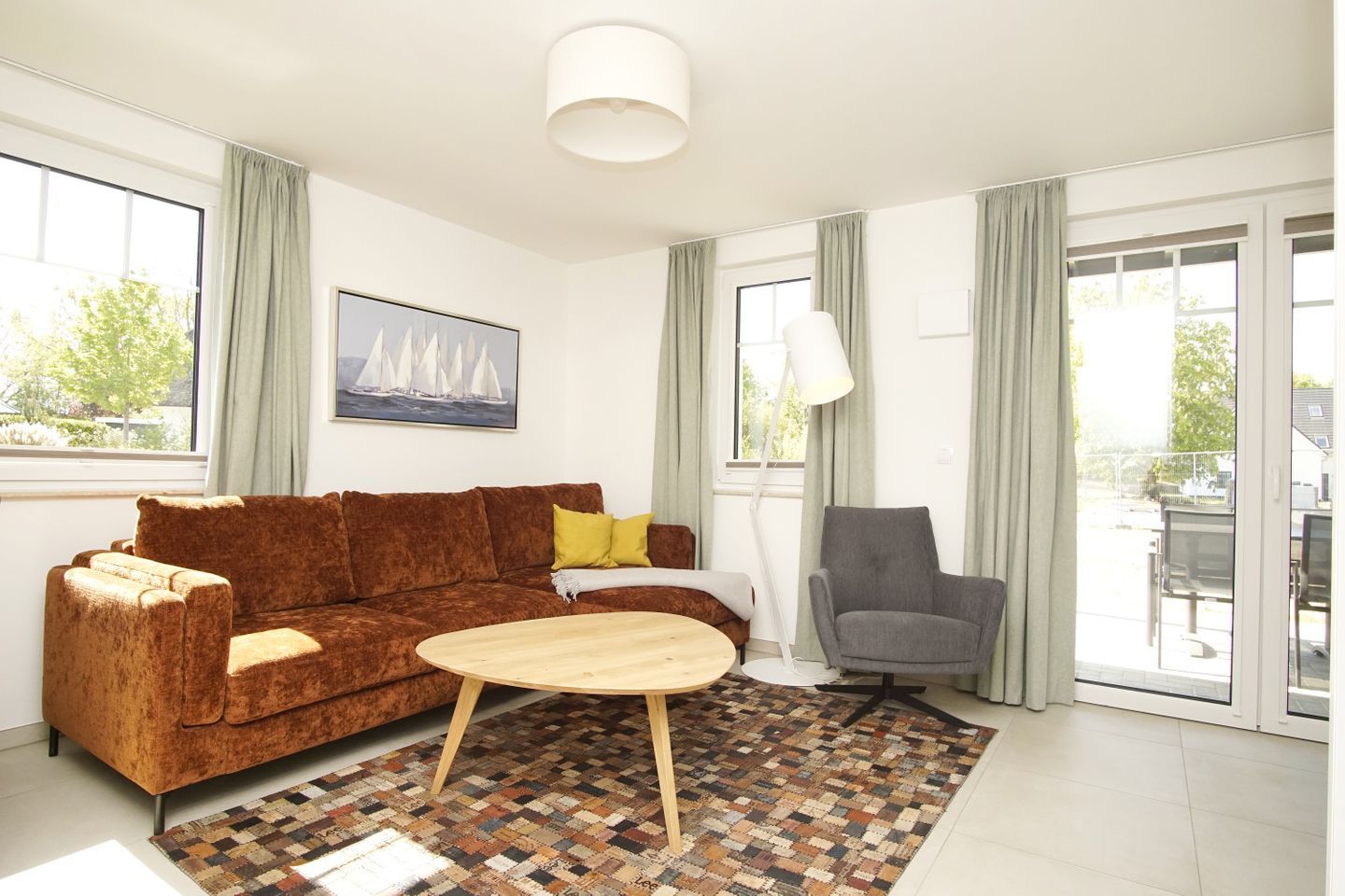 Un salon moderne avec un canapé marron, une table basse ronde en bois, un fauteuil gris et un tapis à motifs.