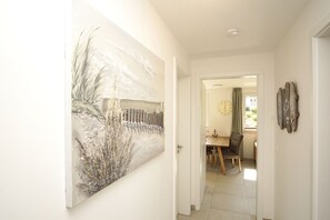 Ein Flur mit einem großen abstrakten Gemälde, ein Essbereich mit Holztisch und -stühlen sowie eine Uhr an der Wand.