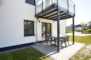 A modern house with a patio, a dining table, and chairs. - Beachfront apartment with terrace, use of swimming pool and sauna - Rex Rugia apartment 15-3 (Göhren)